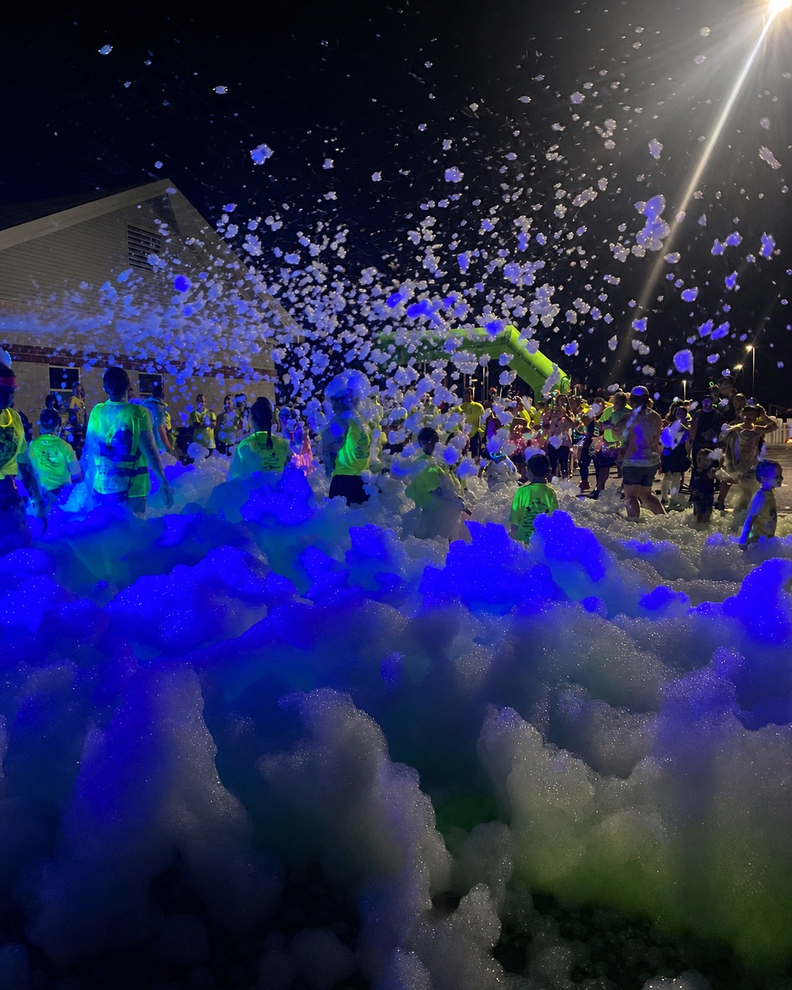 Families enjoying a glowing nighttime foam party with blue and purple foam
